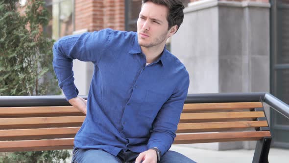 Young Man with Back Pain Sitting Outdoor on bench