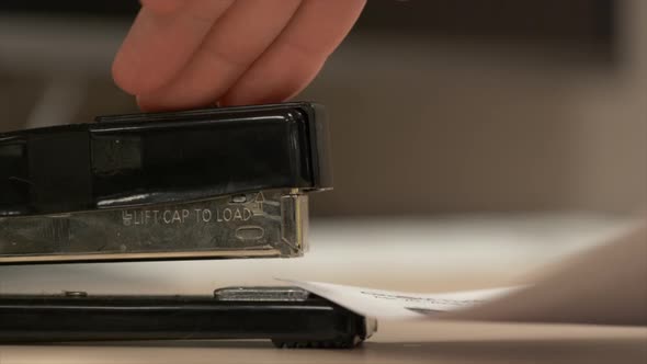 Side view of a black stapler stapling some paper together in really slow motion.