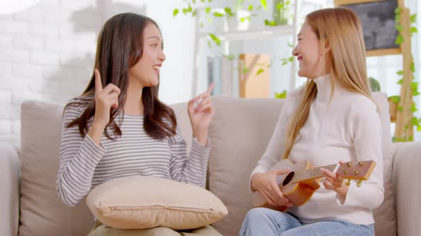 Asian LGBT couple singing and playing guitar musical instrument in living room