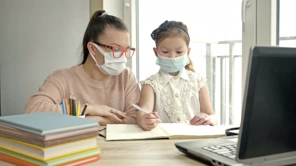 Mom or Teacher or Tutor Helps an Elementary School Student with Her Lessons. Both Have Medical Masks