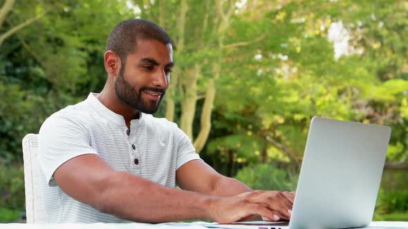 Smiling man using laptop in garden 4k