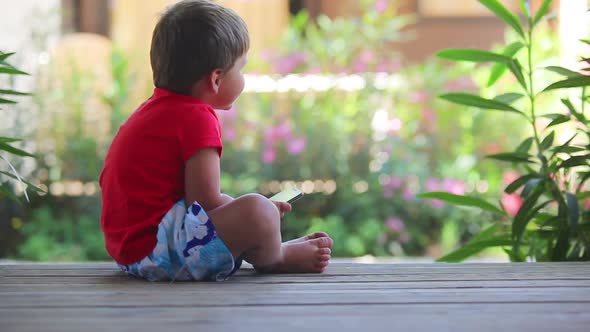 Boy Sits on the Porch and Plays with Mobile Phone