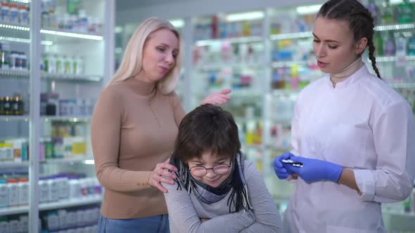 Sad Ill Caucasian Boy with Fever Standing in Drugstore As Woman Consulting Specialist