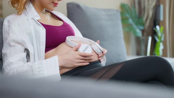 Asian young beautiful pregnant woman applying headphones on her belly.