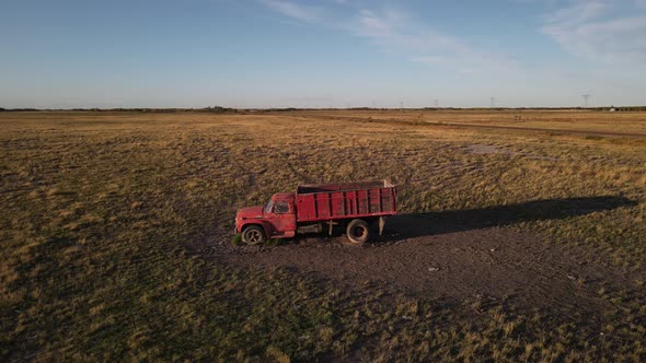 A red old vintage truck standing abandoned in a dry countryside field at sunset. Aerial parallax sho