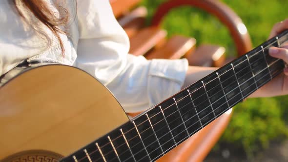 Cute Girl Plays on Guitar on the Bench in the Park