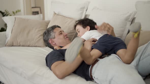 Happy Dad Playing and Romping with Little Son on Couch