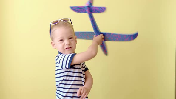 Little Preschool Toddler Child Boy in Blue Tshirt Play with Plastic Foam Airplane on Yellow