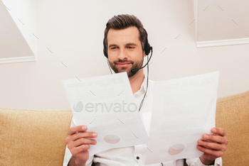 Selective focus of smiling teleworker in headset working with papers at home