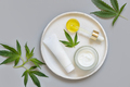 Blank cosmetic tube, jar and pipette near green cannabis leaves on grey. Mockup - PhotoDune Item for Sale