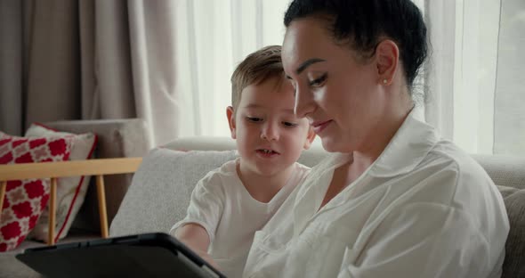 Happy Mom and Cute Son Little Child Mother Plays with Her Baby at Home Relaxing Using Smartphone