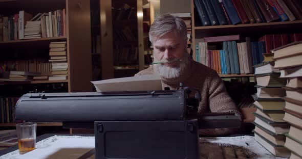 Old american novelist is sitting at the typewriter and doing his work, 4k