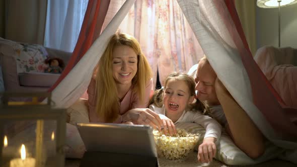 Little Girl and Her Parents Enjoying Watching Cartoons Online in the Tent in the Nursery