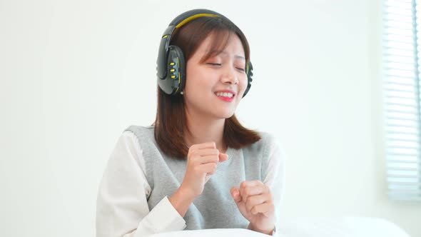 Asian woman listen to music and dance while sitting on bed in bedroom.