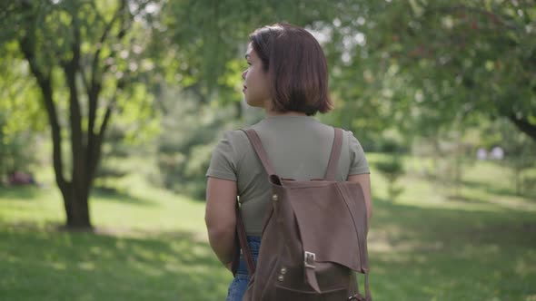 Back View Young Little Woman with Backpack Walking in Sunshine in Spring Summer Forest Looking