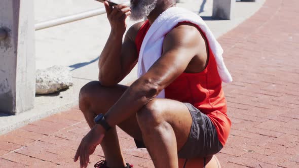 Senior african american man talking on the smartphone while sitting on basketball on the court near