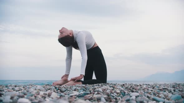 A Woman Doing Exercises for Her Spine on the Pebble Beach