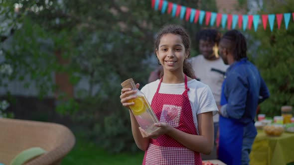 Beautiful Cheerful African American Teenage Girl Posing with Lemon Water on Picnic Outdoors