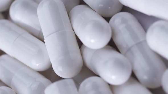 Vertical Video Many White Painkiller Capsules Lie on a White Table and Rotate Closeup