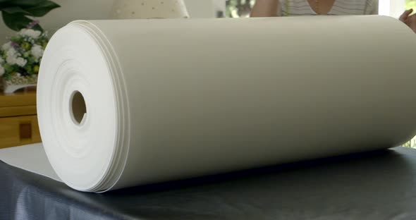 Woman Is Unrolling Large Roll with White Fabric on Table in Fabric Store