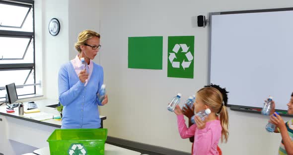 School kids putting bottle in recycle logo box in classroom