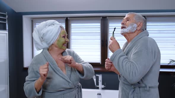 Elderly Grandmother with Facial Green Mask and Grandfather with Shaving Foam Dancing in Bathroom