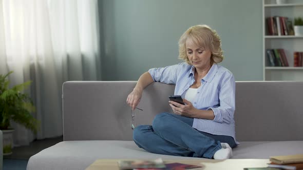 Nice Middle-Aged Woman Sitting on Couch and Scrolling on Smartphone, Application