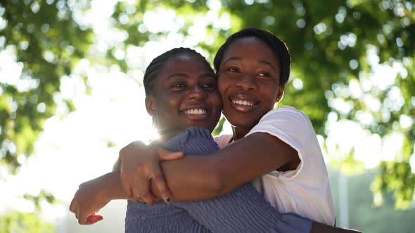 Two Happy Female African American Friends Hugging Looking Away Smiling Standing in Sunlight Outdoors