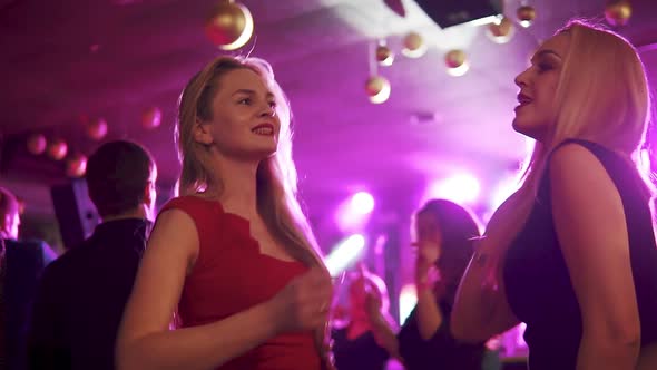 Girlfriends Dancing at a Party in a Crowd of People. Two Blondes Have Fun at the Disco 