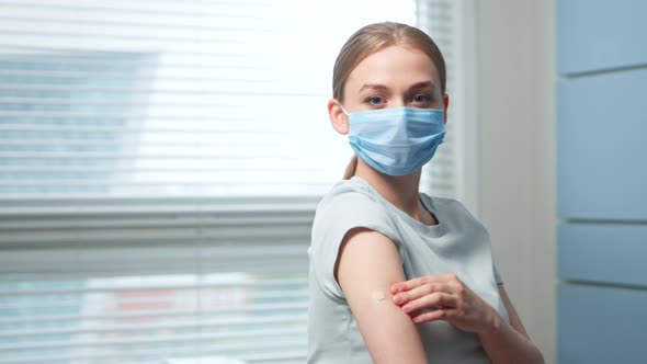 Young woman blonde in blue disposable face mask examines injection spot