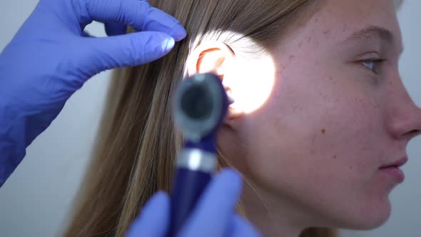 Closeup Side View Ear of Female Teenage Patient with Rack Focus to Otoscope in Doctor Hand