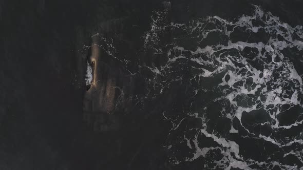 A small wave washing over a barely submerged rock at sunrise AERIAL TOP DOWN