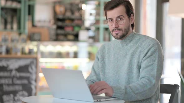 Young Man with Laptop Showing No Sign By Finger in Cafe
