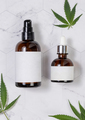 Cosmetic bottles with blank labels near green cannabis leaves on marble table. Mockup - PhotoDune Item for Sale