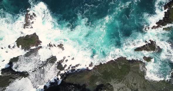Aerial overhead shot sea waves hitting boulder and coral reef in the beach in sunny condition weathe