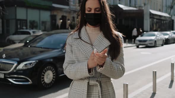 Young Woman with a Black Medical Mask Using Hand Sanitizer on the Street at Day Time