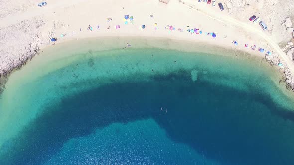 Flying above umbrellas and people on isolated beach of Pag island, Croatia