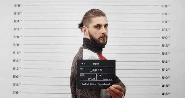 Mugshot of Arrested Bearded Man Turning Head and Looking to Camera While Standing Aside 
