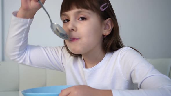 Little Girl Eats Chocolate Corn Balls with Milk Sitting at White Table