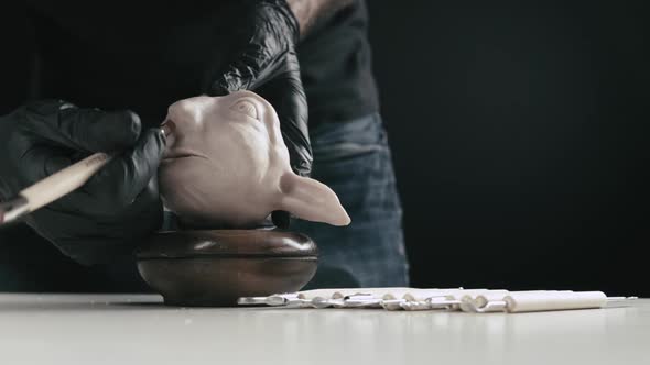 Artist models a plasticine puppet head's nose with a modeling tool