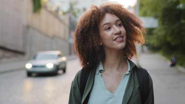 Young Attractive Mixed Race Black Millennial Girl with Afro Hair and Backpack Walking Alone Along