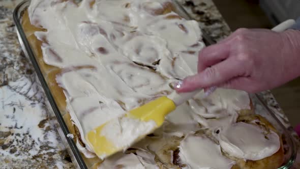 Spreading cream cheese icing on freshly baked cinnamon rolls