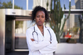 African American female doctor in lab coat with stethoscope posing outside clinic. Medical specialty - PhotoDune Item for Sale