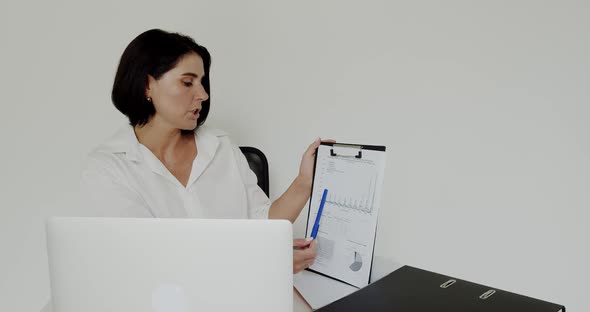 Female Lecturer Chatting on Laptop Using Notebook with Graphics in an Office