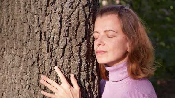 A woman relaxes in nature hugging a tree.