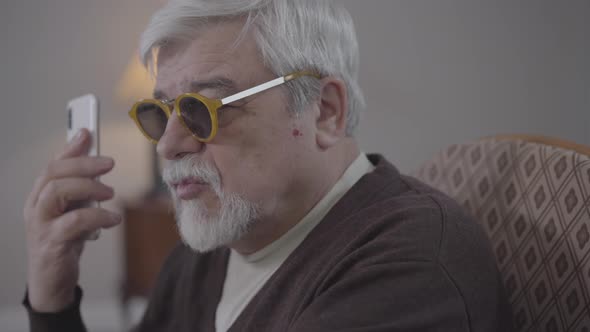 Close-up Side View of Blind Senior Caucasian Man in Eyeglasses Talking on the Phone. Old Male