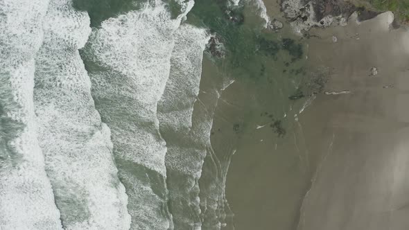 Stationary overhead drone shot of ocean waves coming into beach