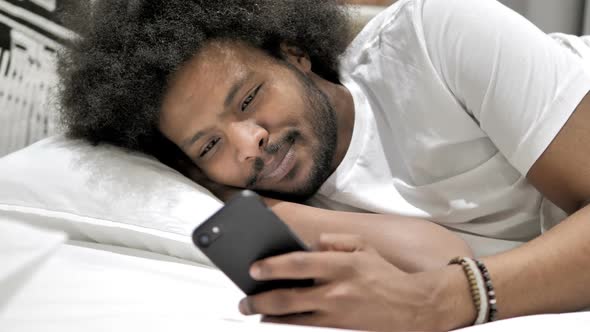 African Man Using Smartphone in Bed