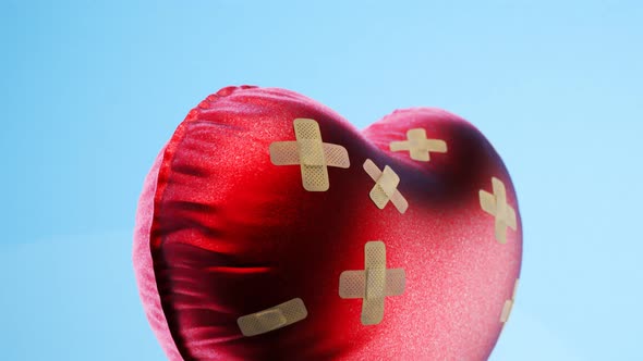 Red heart-shaped balloon fixed with bandaids. Broken heart concept. 4kHD