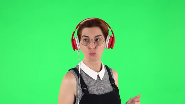 Portrait of Funny Girl in Round Glasses Is Dancing and Enjoying Music in Big Red Headphones. Green